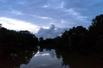 Reflection of silhouette trees in water against sky