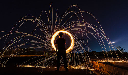 Rear view of man spinning wire wool on field at night