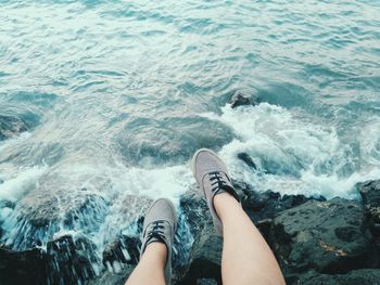 Low section of woman sitting on rocks at beach