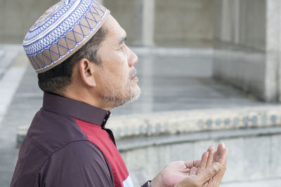 Close-up of mature man praying while sitting at mosque