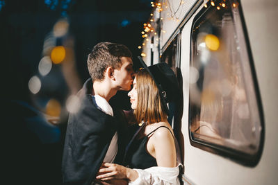 Side view of couple kissing while leaning on van in city