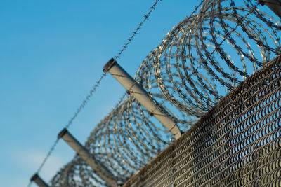 Low angle view of razor wire fence against sky