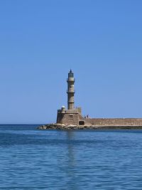 Lighthouse in sea against clear blue sky