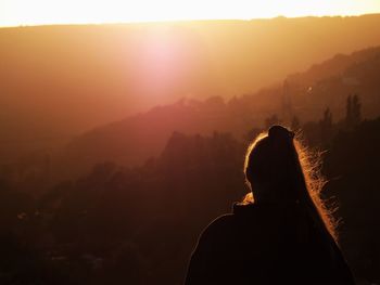 Rear view of woman looking at mountains against sky during sunset