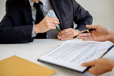 Cropped hands of man giving contract papers for signing to businessman