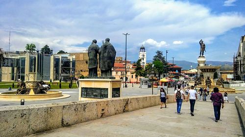 Group of people in city against cloudy sky