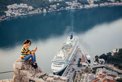 Side view of mid adult woman using mobile phone while sitting on rock against sea