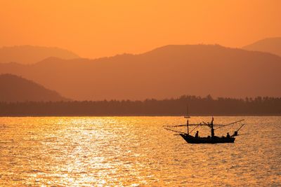 Silhouette boat sailing in sea by mountains against clear sky during sunset