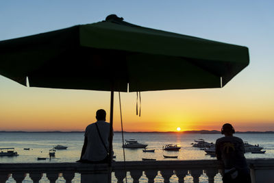 Silhouette people standing by sea against sky during sunset