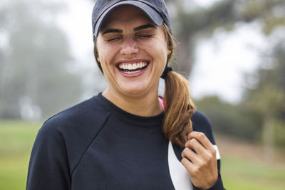 Close-up of cheerful woman with eyes closed wearing cap and sports clothing at park