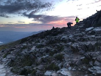 People on rock against sky during sunset