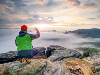 Man standing on rock against sky during sunset