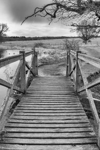 Wooden footbridge on footpath by water against sky