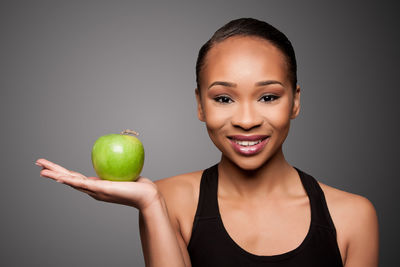 Portrait of smiling young woman holding apple against black background