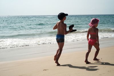 Rear view of shirtless boy walking on beach against clear sky