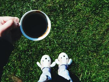 Low section of woman with coffee standing on grassy field