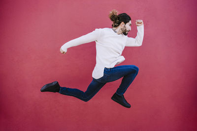 Full length of young woman jumping against red wall