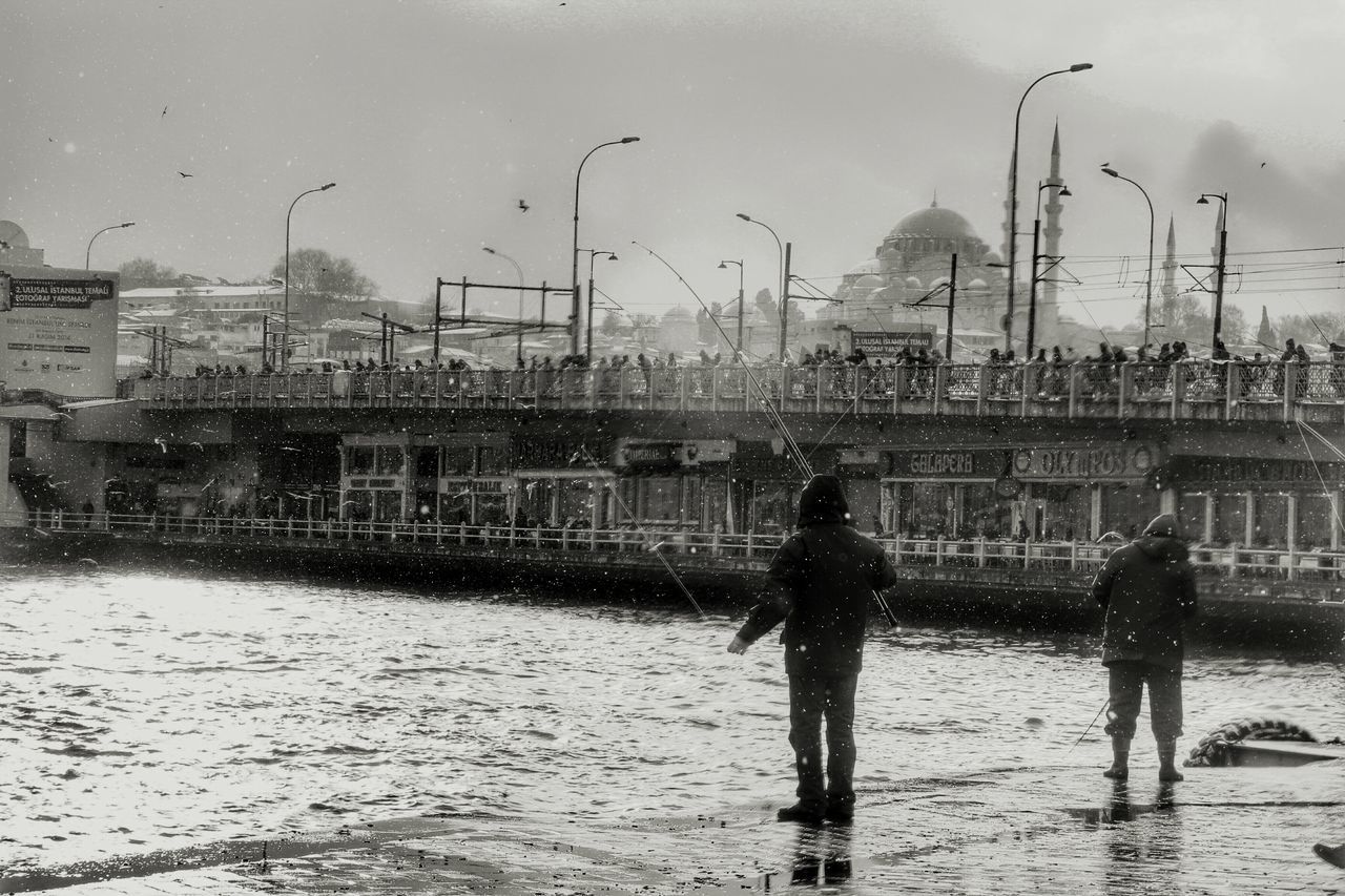 water, lifestyles, sky, building exterior, built structure, leisure activity, architecture, men, person, reflection, standing, full length, cloud - sky, city, rear view, weather, outdoors