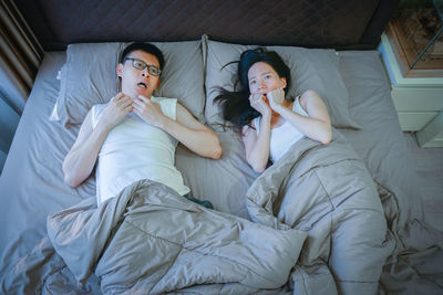 High angle view of scared couple lying on bed at home