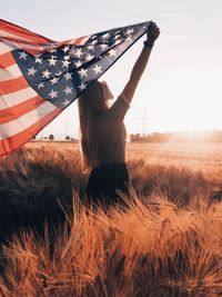 Woman with arms raised on field against sky during sunset