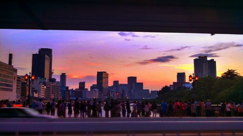 Crowd in city against sky during sunset