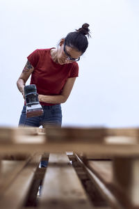 Young woman polishing a wooden plank with a power sander