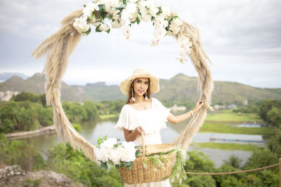 Portrait of smiling young woman standing by plants in basket