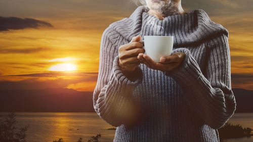 Woman holding coffee cup against orange sky