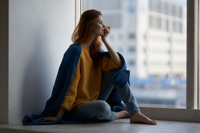 Young woman looking away while sitting on floor at home
