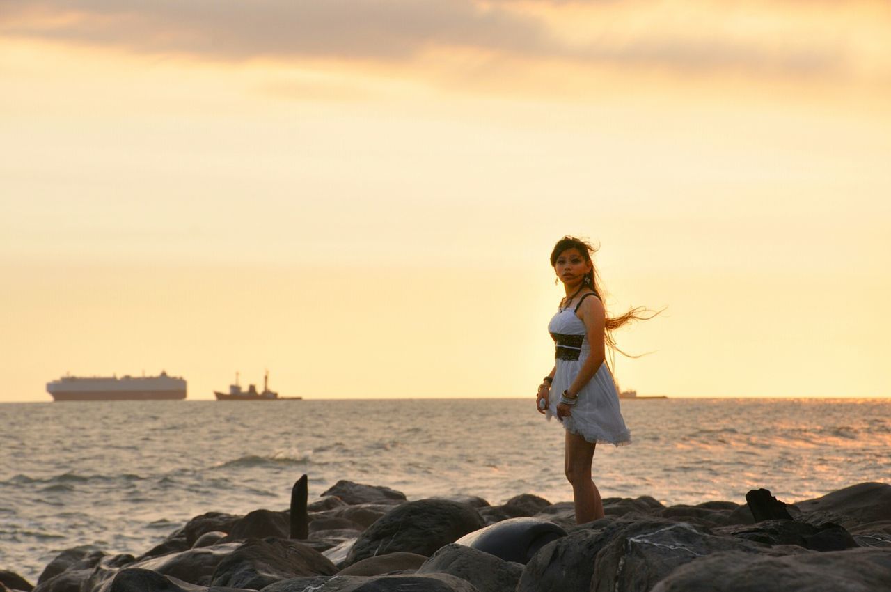 sea, horizon over water, water, lifestyles, full length, leisure activity, sky, standing, beach, casual clothing, shore, beauty in nature, young adult, scenics, tranquility, nature, tranquil scene, rock - object