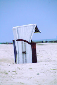 Hooded chair at beach against clear sky