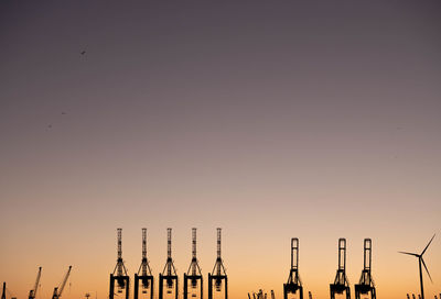 Silhouette cranes at construction site against clear sky during sunset