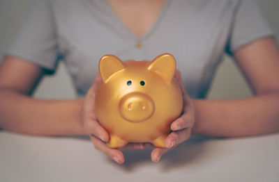 Midsection of woman holding piggy bank on table