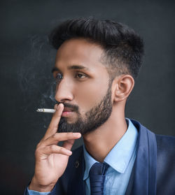 Young man smoking cigarette against black background