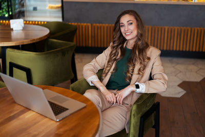 Portrait of young woman using phone while sitting on table