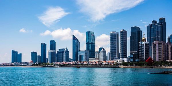 Modern buildings by river against cloudy sky