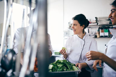 Male and female chefs discussing over leaf vegetable in commercial kitchen