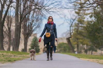 Woman walking with dog on road amidst trees during winter