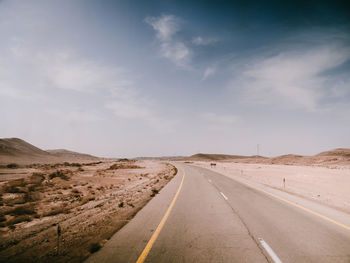 Diminishing perspective of empty road by landscape against sky