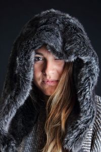 Portrait of woman wearing fur coat against black background