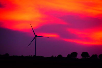 Silhouette of wind turbines on field during sunset