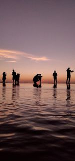 Silhouette people on sea against sky during sunset