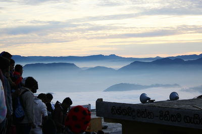 People looking at mountains in foggy weather against sky