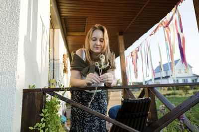 Woman holding twig of globe thistle while leaning on railing