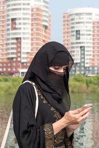 A muslim woman in national clothes with her face covered with a phone in her 