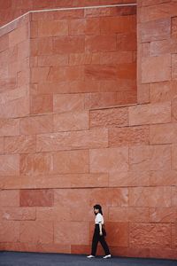 Side view of woman standing against brick wall