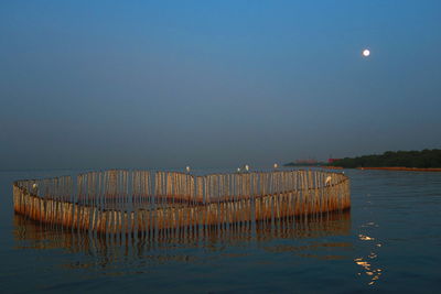 Wooden posts in sea against clear sky at night