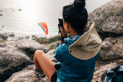 High angle view of woman photographing while sitting on rock