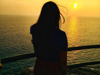 Rear view of woman looking at sea during sunset