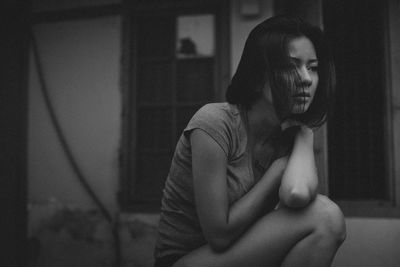 Thoughtful young woman looking away while sitting by house